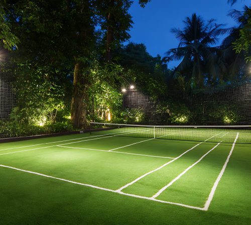 nighttime tennis court glows under lush green lighting.
